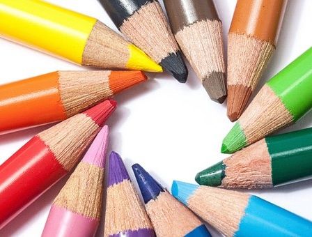 Eine Sammlung von Buntstiften, die in einem kreisförmigen Muster auf einem weißen Hintergrund angeordnet sind. Die Stifte haben verschiedene Farben, darunter Gelb, Orange, Rot, Pink, Lila, Blau, Grün und Braun.