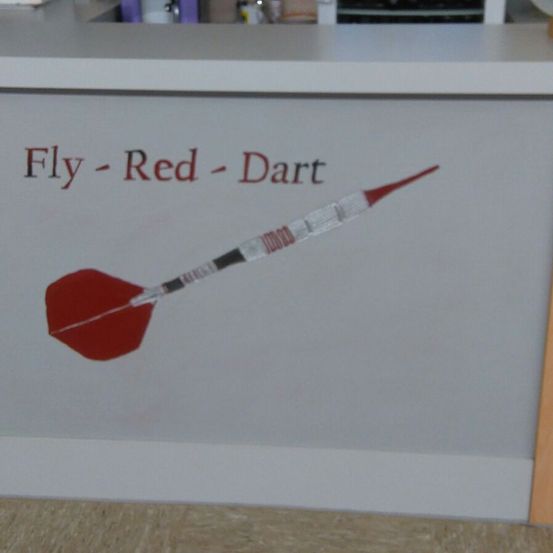 Eine weiße Wand mit rotem Text 'Fly - Red - Dart' und einem roten Pfeil mit roter Spitze und silbernem Schaft, der daran befestigt ist.