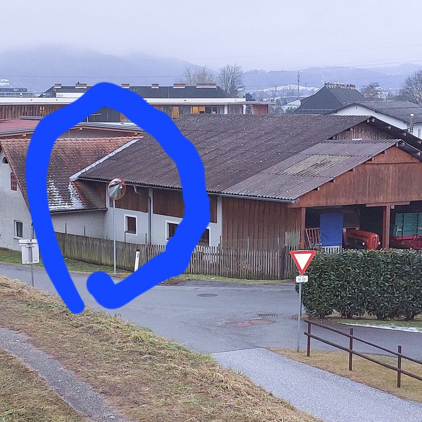 Ein blauer Kreis umrahmt ein kleines Wohngebiet mit einem braunen Haus, einem roten Auto in der Garage und einem dreieckigen Straßenschild.