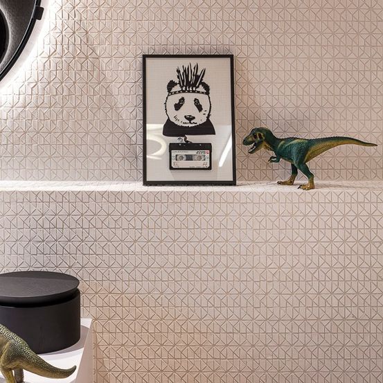 Eine gemusterte Wand mit einem Regal zeigt ein gerahmtes Bild eines Pandas und eine Dinosaurier-Spielzeugfigur. Ein rundes schwarzes Objekt und eine weitere Dinosaurier-Spielzeugfigur befinden sich auf dem Regal und dem Tisch.