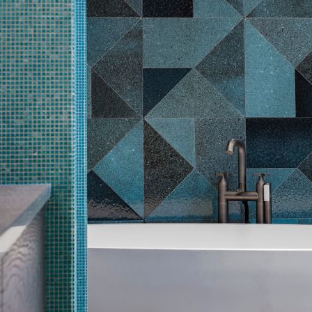 Ein modernes Badezimmer mit türkisen und schwarzen Rautenfliesen an der Wand und einer weißen Badewanne mit bronzefarbenem Wasserhahn.