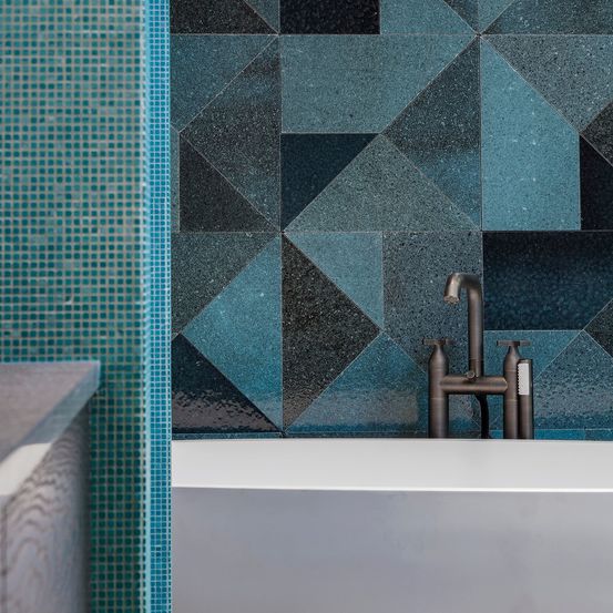 Ein modernes Badezimmer mit türkisen und schwarzen Rautenfliesen an der Wand und einer weißen Badewanne mit bronzefarbenem Wasserhahn.