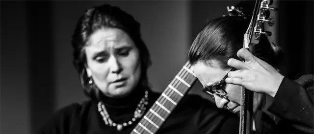 Zwei Frauen spielen Gitarren, eine Frau mit geschlossenen Augen, die andere Frau mit offenen Augen, konzentriert auf ihr Instrument schauend.