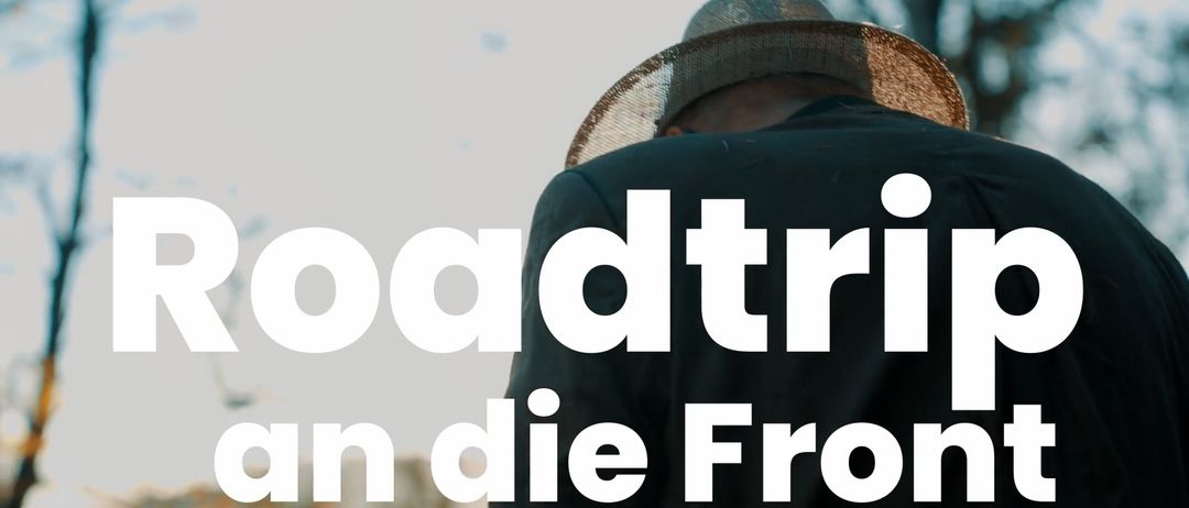Eine Person mit einem Strohhut steht vor einem unscharfen Hintergrund. Der Text 'Roadtrip' ist in Weiß auf schwarzem Hintergrund geschrieben.