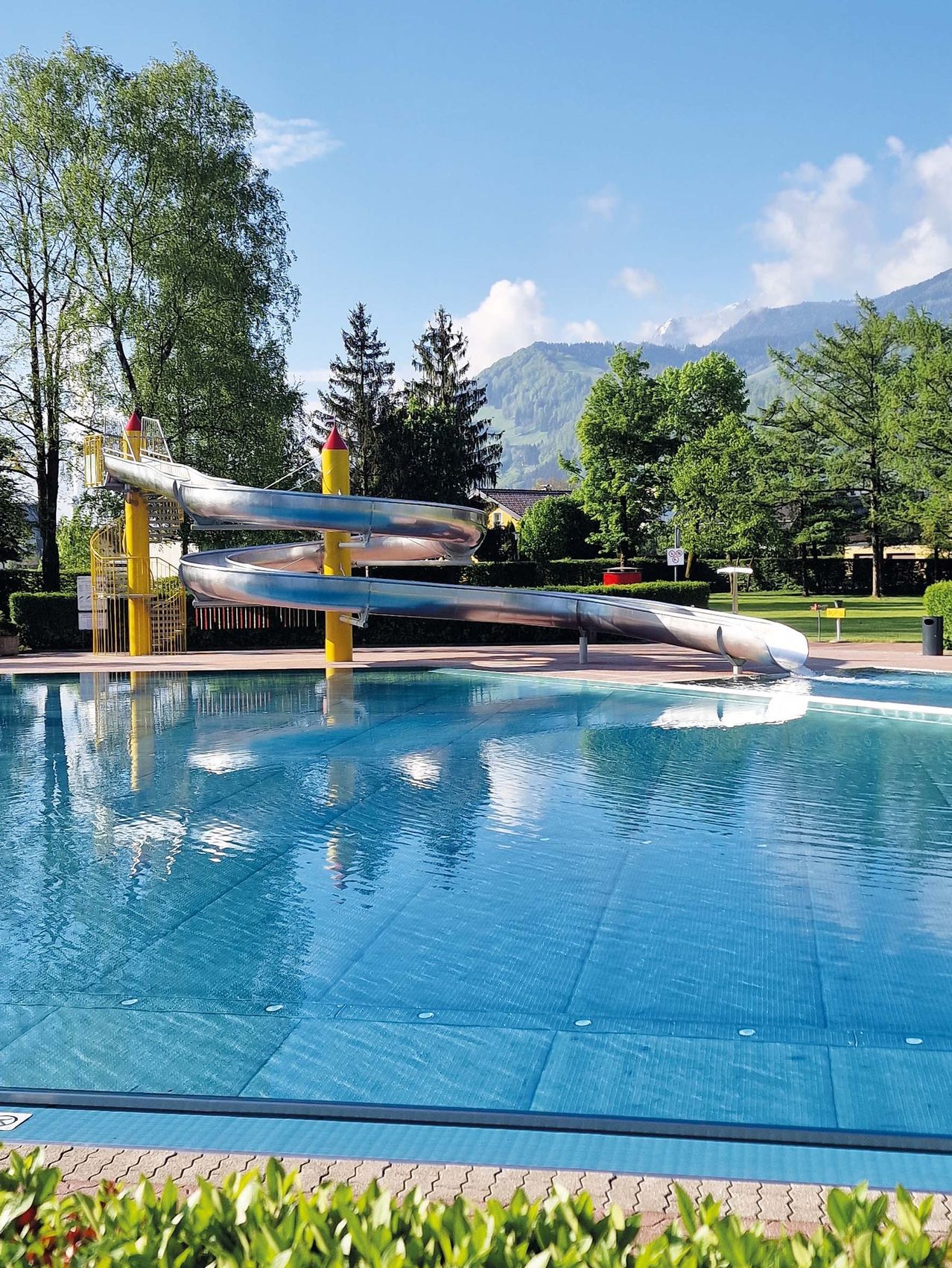 Außenpool mit einer großen Rutsche und Bergen im Hintergrund.