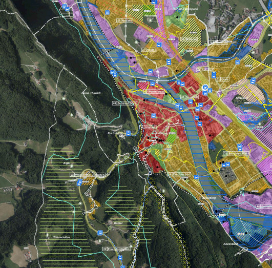 Luftbildkarte, die verschiedene Landnutzungen wie Wohn-, Gewerbe- und Grünflächen zeigt. Straßen, Bahnen und ein Fluss sind hervorgehoben. Die Karte ist in Abschnitte mit farbigen Überlagerungen unterteilt.