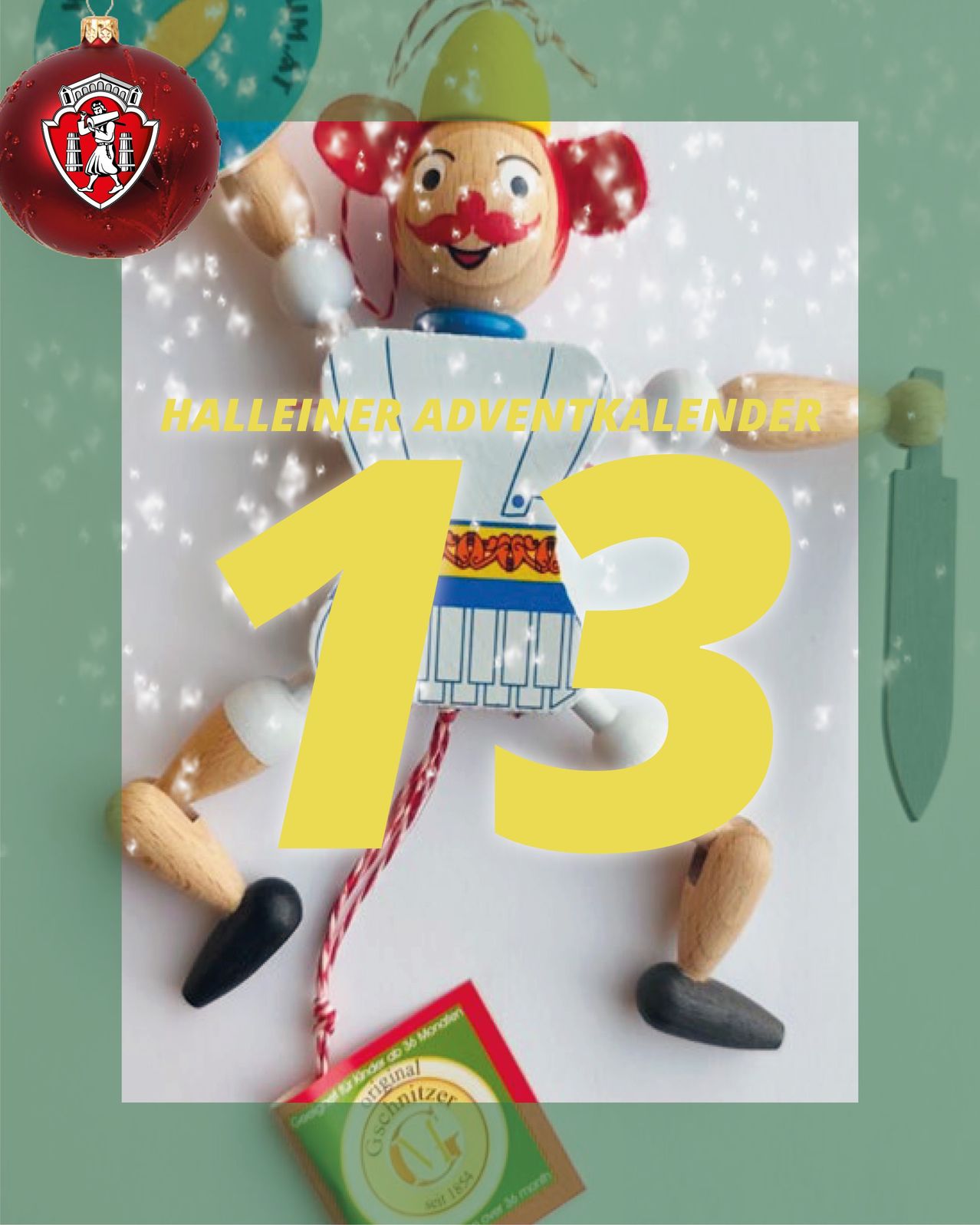 Ein hölzerne Clown mit roter Nase und blau-weißem Kostüm steht auf einer weißen Oberfläche. Die Nummer 13 ist prominent in Gelb angezeigt. Es gibt einen roten Ball und einen roten und grünen Schmuck.