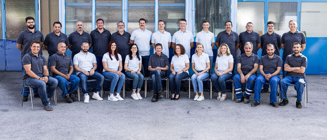 Ein Team von Mitarbeitern in einheitlichen Kleidungsstücken posiert für ein Gruppenfoto vor einem blauen Gebäude.