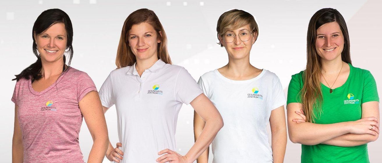 Drei Frauen, alle in weißen Shirts, posieren für ein Foto. Sie haben die Hände auf den Hüften und lächeln. Die Shirts haben Logos darauf.
