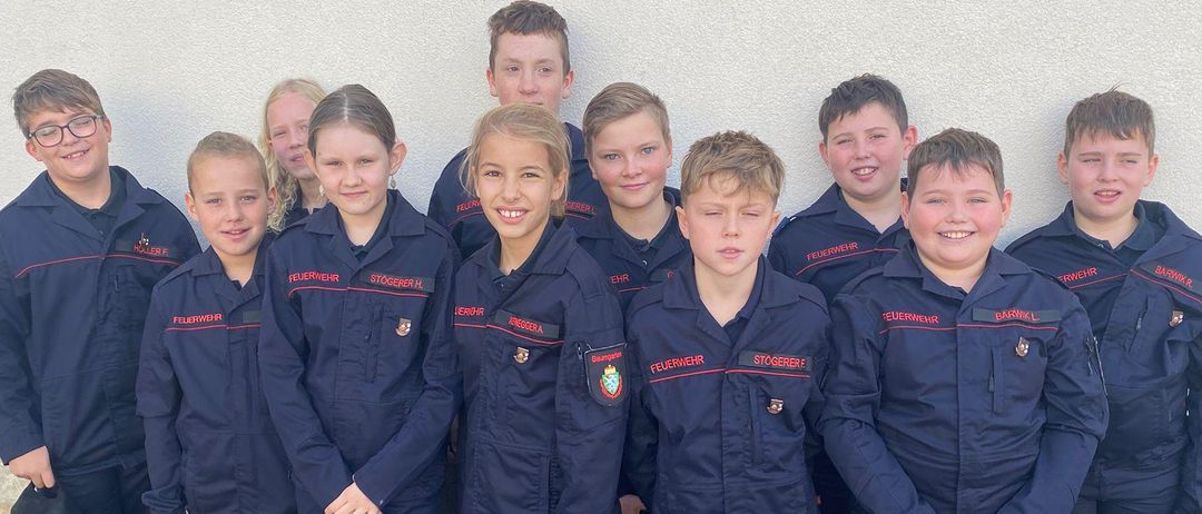 Eine Gruppe junger Personen, die gleiche dunkelblaue Uniformen tragen, posiert für ein Foto. Sie stehen vor einer hellen Wand, mit ihren Händen in verschiedenen Positionen.