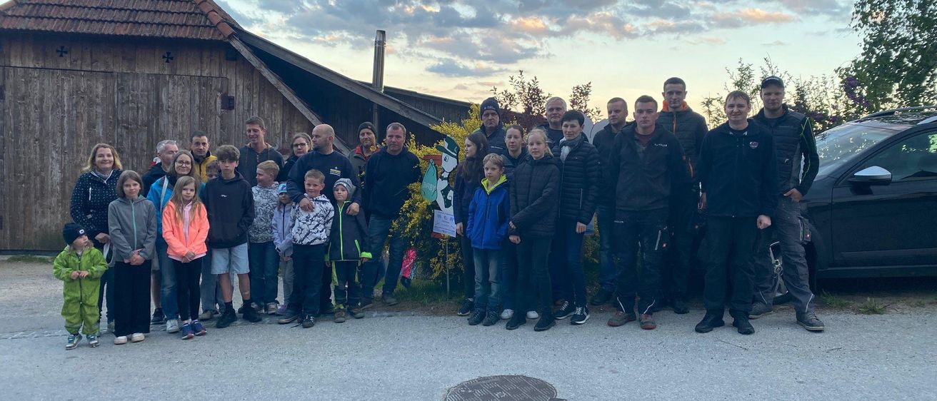 Eine Gruppe von Menschen, sowohl Erwachsene als auch Kinder, stehen draußen und posieren für ein Foto vor einem rustikalen Gebäude unter einem bewölkten Himmel.