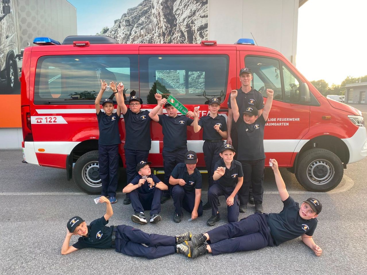 Eine Gruppe junger Feuerwehrleute in Uniform posiert für ein Foto vor einem Feuerwehrwagen.