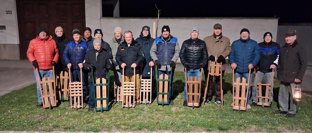 Eine Gruppe von Männern posiert nachts für ein Foto, hält Schlitten und hat ein Gebäude und eine Satellitenschüssel im Hintergrund.