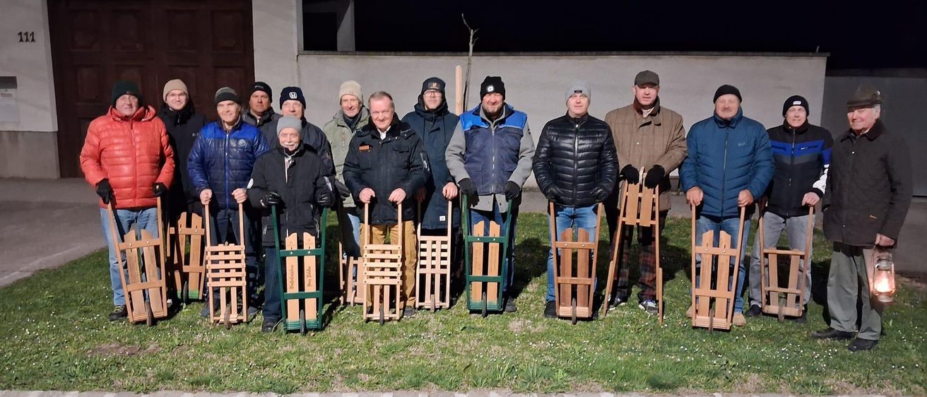 Eine Gruppe von Männern posiert nachts für ein Foto, hält Schlitten und hat ein Gebäude und eine Satellitenschüssel im Hintergrund.