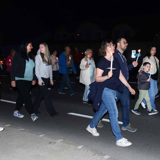 Eine Gruppe von Menschen mit brennenden Kerzen geht bei Nacht die Straße entlang.