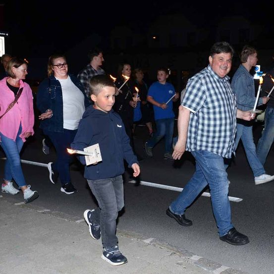 Eine Gruppe von Menschen, die bei Nacht auf der Straße geht und brennende Kerzen hält. Sie tragen Freizeitkleidung.