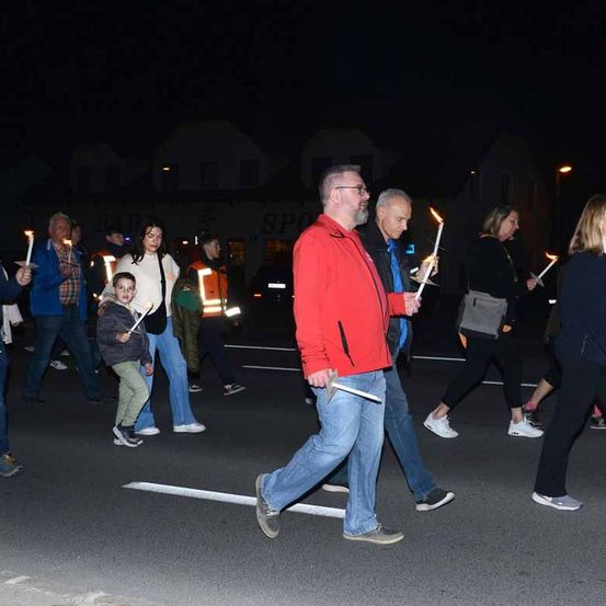 Eine Gruppe von Menschen läuft bei Nacht mit brennenden Kerzen auf der Straße.