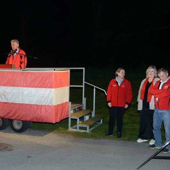 Ein Mann spricht bei Nacht an einem Rednerpult mit einem rot-weißen Flaggenhintergrund.