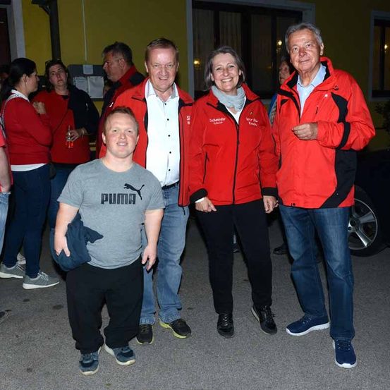 Eine Gruppe von Menschen in roten Jacken und einem Mann in einem Puma-Shirt stehen zusammen auf einer Straße.