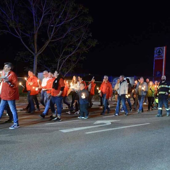 Eine Gruppe von Menschen in orangefarbenen Hemden mit Kerzen in der Hand marschiert bei Nacht auf der Straße.