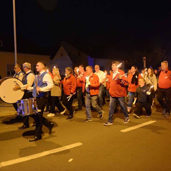 Eine Gruppe von Menschen marschiert bei Nacht auf der Straße und hält brennende Kerzen. Einige spielen Trommeln.