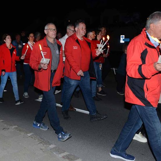 Eine Gruppe von Menschen geht bei Nacht die Straße entlang und hält brennende Kerzen in den Händen.