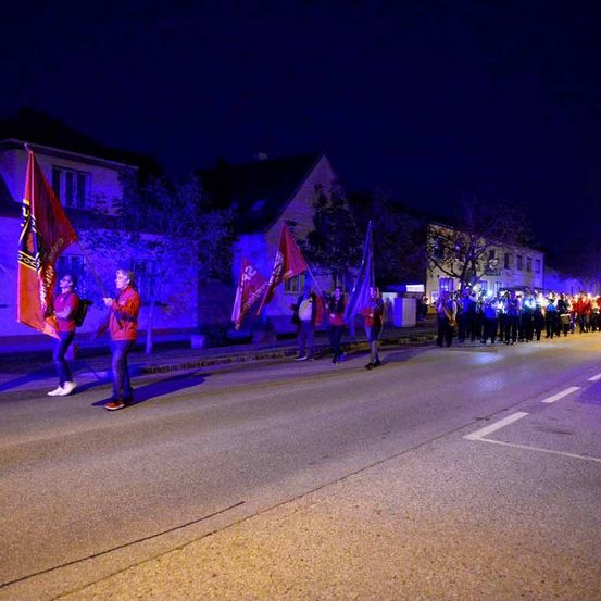 Eine Gruppe von Menschen marschiert nachts auf der Straße und hält Flaggen.