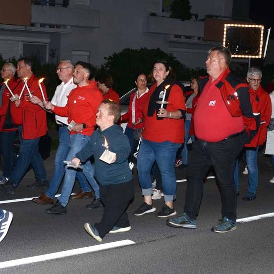 Eine Gruppe von Menschen in Rot geht bei Nacht auf der Straße und hält Kerzen in den Händen.