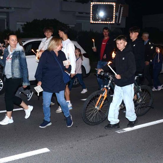 Eine Gruppe von Menschen mit Kerzen überquert bei Nacht die Straße, einige sind auf Fahrrädern.