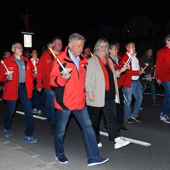 Eine Gruppe von Menschen in roten Jacken zieht nachts bei einer Parade. Sie halten brennende Kerzen in den Händen.