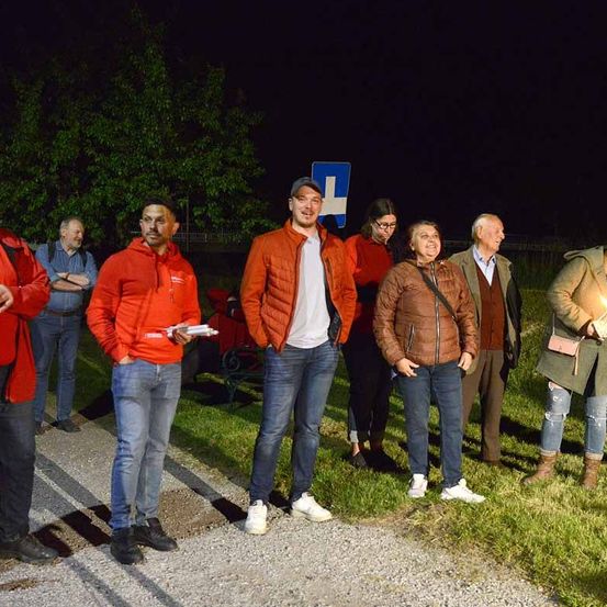 Eine Gruppe von Menschen steht bei Nacht draußen. Eine Frau hält eine brennende Kerze.