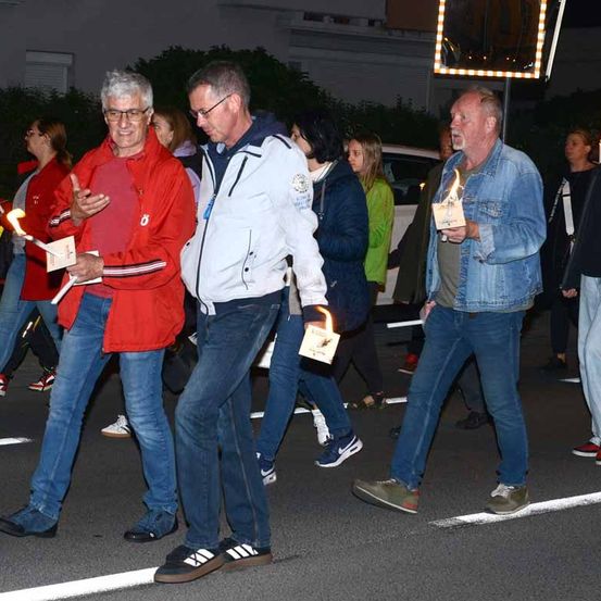 Männer mit brennenden Kerzen gehen nachts mit anderen hinter ihnen laufenden Leuten eine Straße entlang.