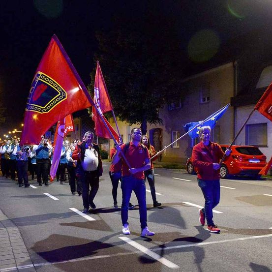 Menschen marschieren bei Nacht auf der Straße mit Flaggen und Musikinstrumenten.