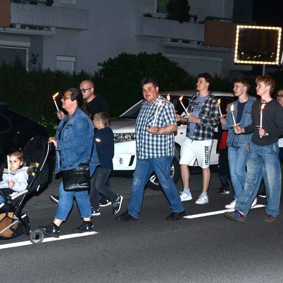Eine Gruppe von Menschen, einschließlich Kindern, halten Kerzen und gehen bei Nacht eine Straße entlang.