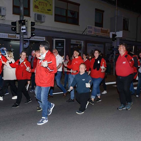 Gruppe von Menschen, die mit Kerzen in der Hand die Straße entlanggehen. Sie tragen rote Jacken.