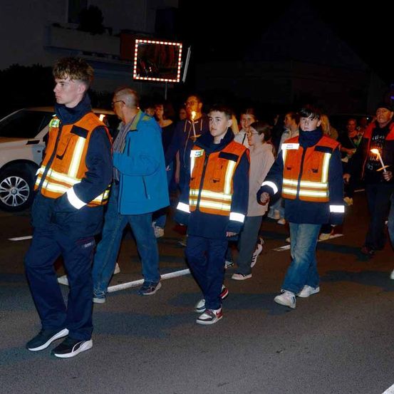 Eine Gruppe von Menschen in Sicherheitswesten geht nachts auf der Straße und hält Kerzen in den Händen.