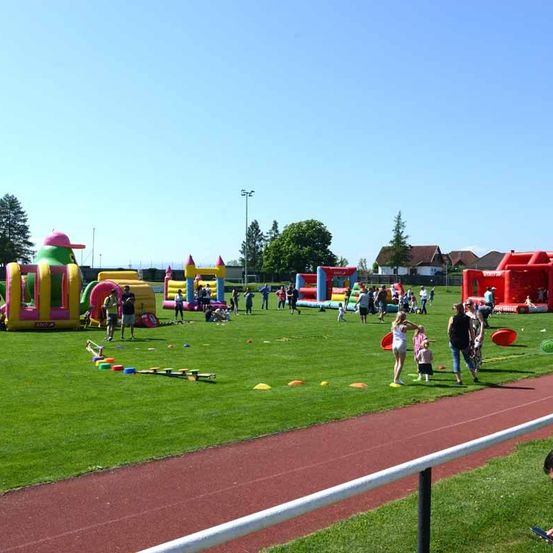 Ein Außenbereich mit Kindern, die an einem sonnigen Tag auf aufblasbaren Spielzeugen und Hindernissen spielen.