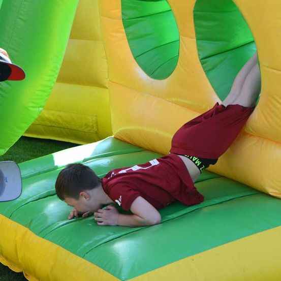 Ein junger Junge in einem roten Shirt kriecht durch einen bunten aufblasbaren Rutschen mit grünen und gelben Farben.