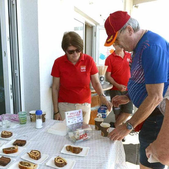 Eine Person in einem roten Shirt gießt ein Getränk aus einer Box in einen Becher. Es sind mehrere Leute um den Tisch herum.