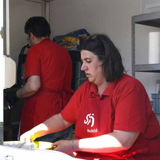 Zwei Arbeiter in roten Uniformen sind in einem Food-Truck, einer von ihnen konzentriert sich auf die Reinigung eines gelben Behälters.