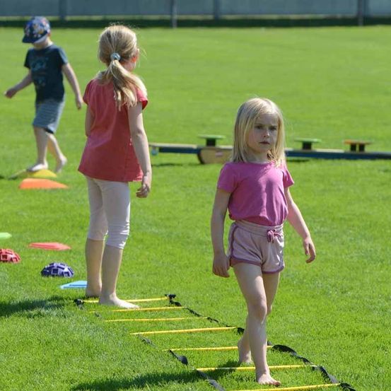 Drei Kinder spielen auf einem Feld. Zwei Mädchen stehen auf den Hürden und ein Junge geht in der Nähe der Frisbees.