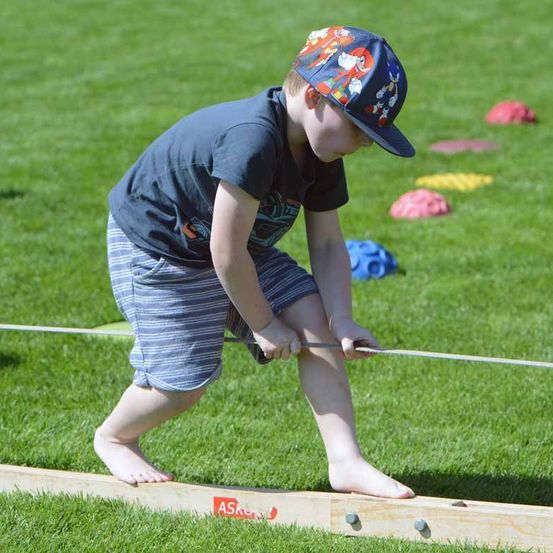 Ein junger Junge in einem blauen Shirt und einer Kappe zieht eine Schnur auf einem Rasenfeld im Freien.
