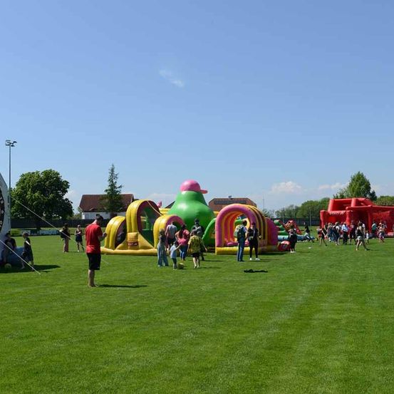 Mehrere Kinder spielen auf dem großen aufblasbaren Spielplatz auf dem Rasen.