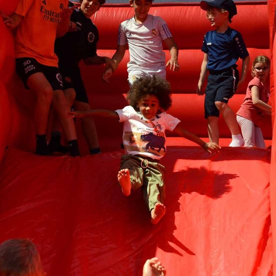 Kinder spielen in einem aufblasbaren Haus mit rotem Boden und Wänden. Ein Kind rutscht herunter.