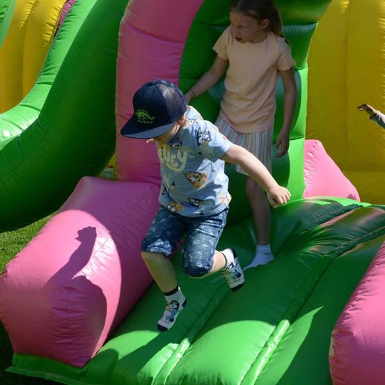 Zwei Kinder spielen auf einem aufblasbaren Hindernisparcours. Ein Junge läuft die Rutsche hoch, während ein Mädchen zuschaut.