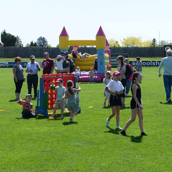 Eine Gruppe von Menschen spielt auf einem Feld. Ein Kind spielt mit einer Wasserpistole, und einige stehen in der Nähe des aufblasbaren Schlosses. Eine Person hält ein Kind auf dem Springschloss.