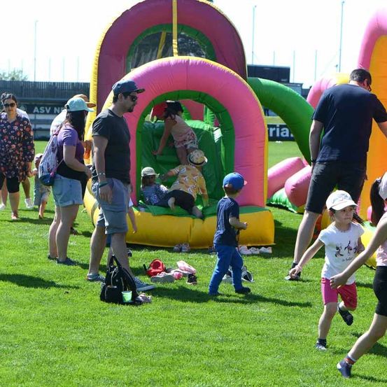 Eine Gruppe von Menschen, darunter Kinder, befindet sich in einem Park mit aufblasbaren Spielen und Aktivitäten.