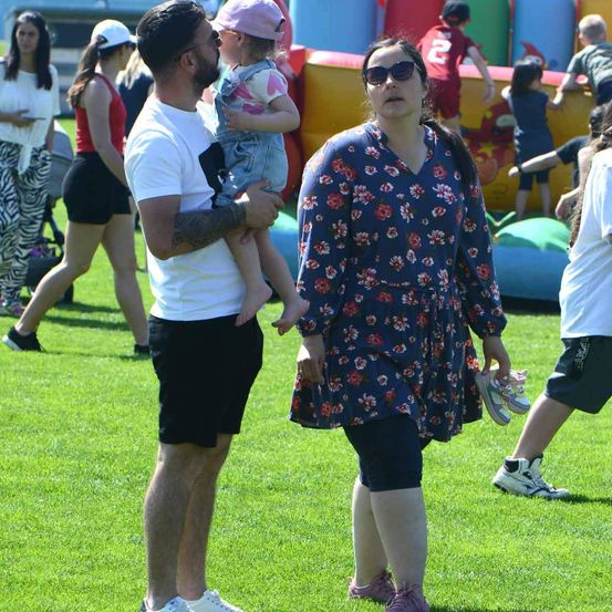 Eine Familie läuft auf einem Rasenfeld, im Hintergrund befindet sich ein bunter aufblasbarer Hindernisparcours.