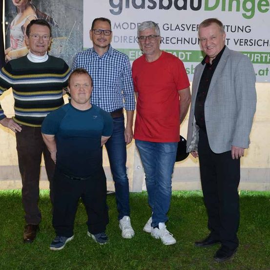 Fünf Männer stehen vor einem Banner der Firma 'Glasbau Dinge', sie lächeln und scheinen für ein Foto zu posieren.