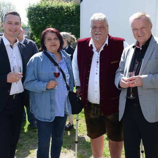 Vier Personen posieren für ein Foto bei einer Veranstaltung. Ein Mann im Anzug, eine Frau in einer Jeansjacke und zwei Männer in Westen.
